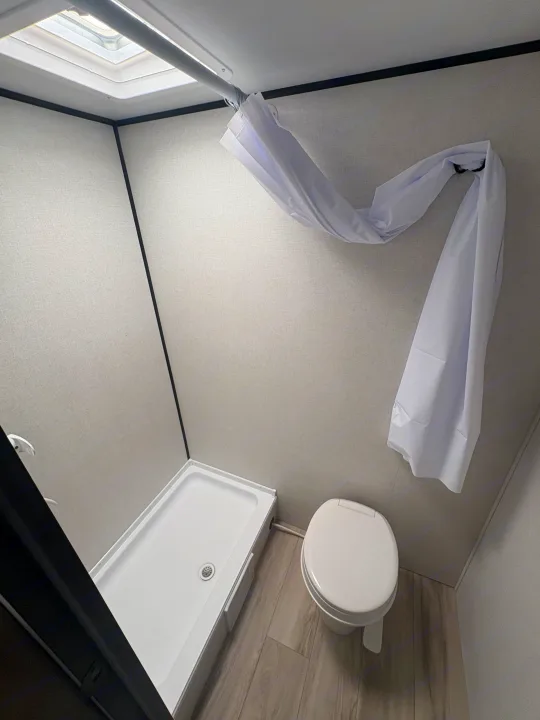 Inside an RV rental: Bright, compact bathroom with white shower and toilet. Features a skylight & clean design.. Keystone RV Coleman 2025