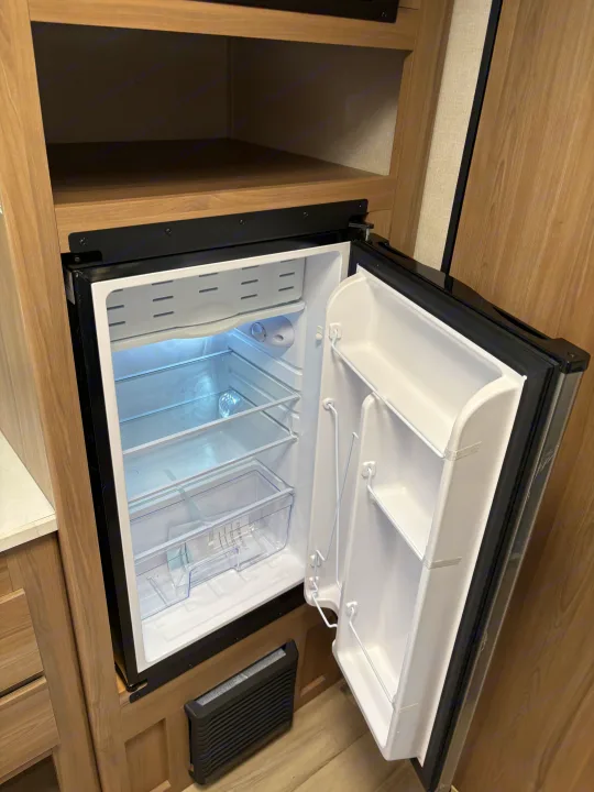 RV rental: Brightly lit, open and empty compact refrigerator with interior shelves and freezer compartment, ready for use.. Keystone RV Coleman 2025