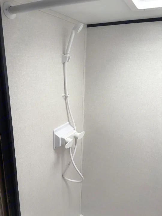 RV rental shower features a handheld shower head, minimalist controls, and textured light gray walls.. Keystone RV Coleman 2025