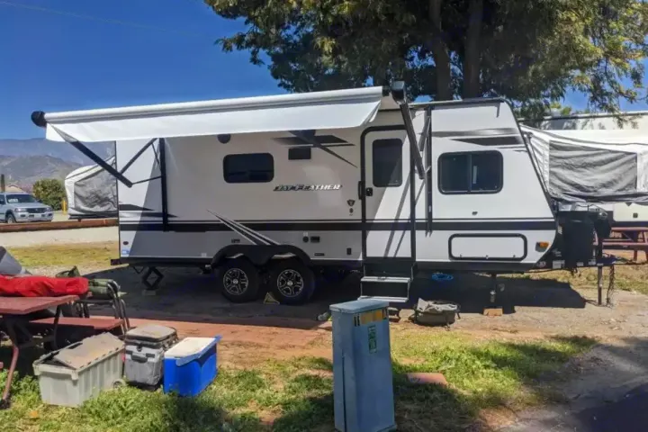 A white Jay Feather travel trailer, an RV rental, is parked at a sunny campsite with its awning extended.. Jayco Jay Feather 2021