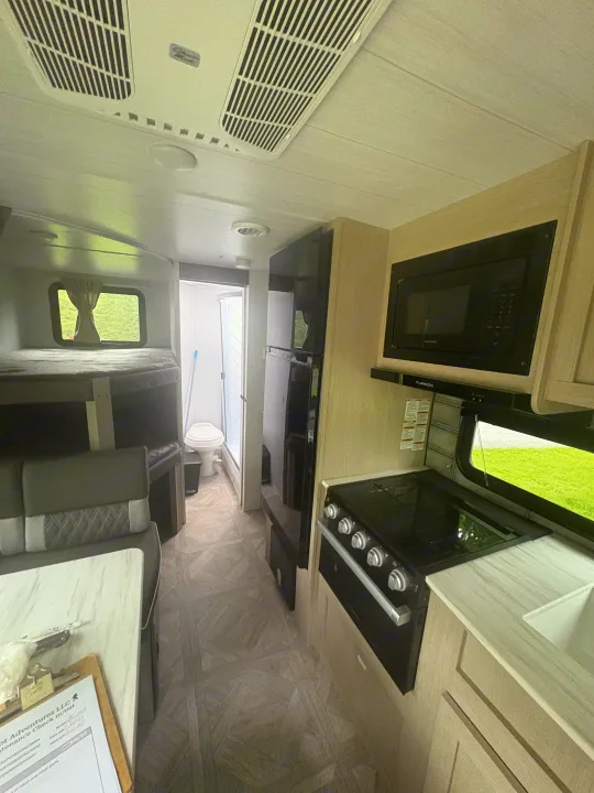 Explore this comfy RV rental interior: kitchen with stove & microwave, bunks, dinette, and bath.. Forest River Wildwood X-Lite 2023