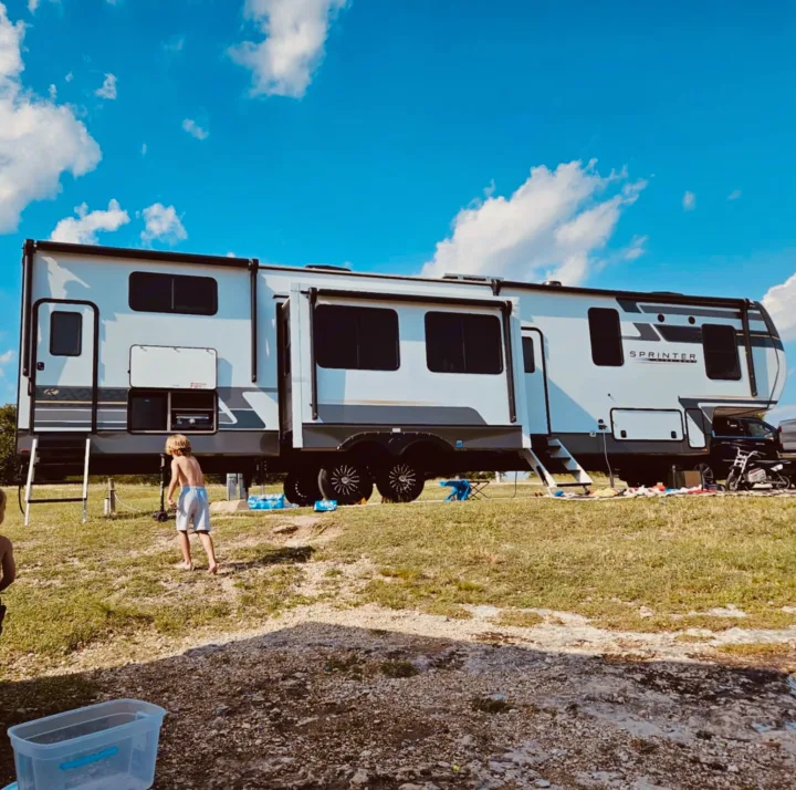 Family fun with an RV rental! A large Sprinter travel trailer is parked outdoors with kids playing near it under a blue sky.. Keystone Sprinter Wide Body 2025