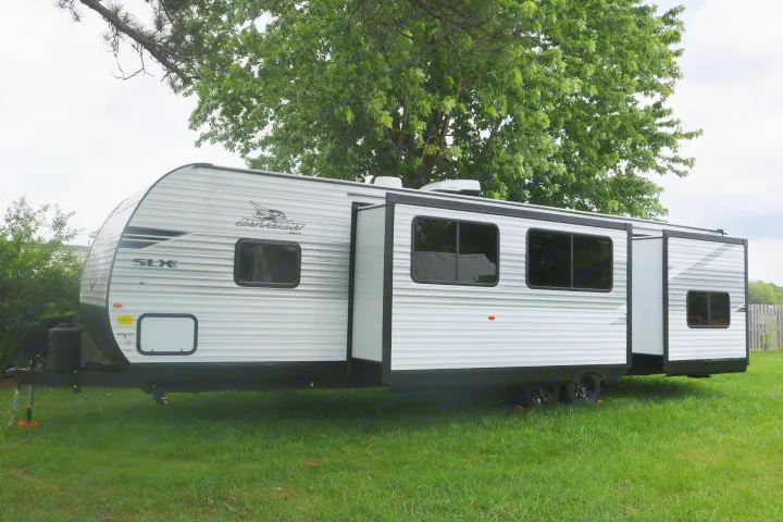 This white Jay Flight SLX travel trailer, ideal for an RV rental, is parked on green grass with a large tree in the background.. 1UJBC0BT8S1YT0519 321BDS 2025