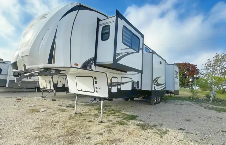 This spacious white fifth-wheel RV rental is parked with extended slide-outs on a gravel lot, ready for your travel adventures.. Forest River Sabre 2021