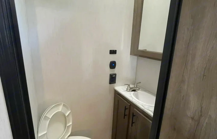 This RV rental features a compact bathroom with a toilet, sink, mirror, and wall-mounted controls.. Forest River Sabre 2021