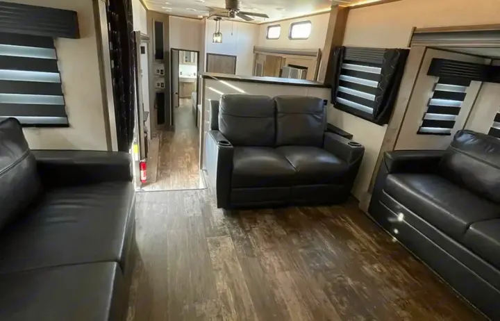 Step into this modern RV rental's living space, featuring comfy black leather sofas, wood floors, and well-lit windows.. Forest River Sabre 2021