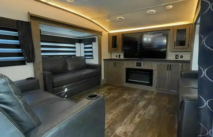 Spacious RV rental living area with black sofas, a large TV, and fireplace, creating a cozy and modern interior.. Forest River Sabre 2021