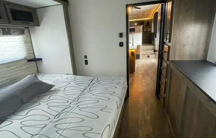 Inside this rv rental: cozy bedroom with patterned bed, opening to a modern kitchen and stepped living area. Perfect for your adventures.. Forest River Sabre 2021