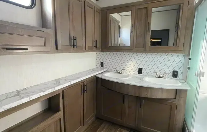 Well-appointed RV rental bathroom with dual sinks, sleek wood-grain cabinetry, and stylish marble-look countertops.. Forest River Sabre 2021