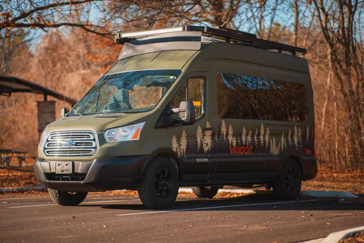 Olive green Ford Transit camper van, an ideal rv rental for your next adventure. Features tree graphics & roof rack.. Vandoit LIV 2019