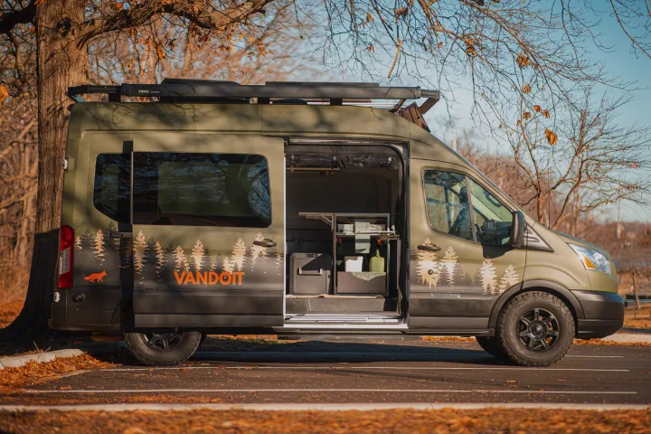 Olive green custom RV rental camper van with open door, showing organized interior, roof rack, and forest graphics for adventure.. Vandoit LIV 2019