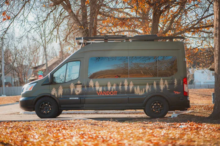 Side profile of a green VANDOIT camper van RV rental, with tree graphics. Parked among autumn trees, ready for adventure.. Vandoit LIV 2019