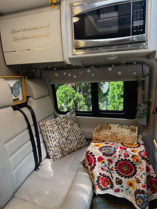 Inside a welcoming RV rental: comfy seating, microwave, colorful decor, and a window view of trees.. Thor Motor Coach 18A Rize 2023