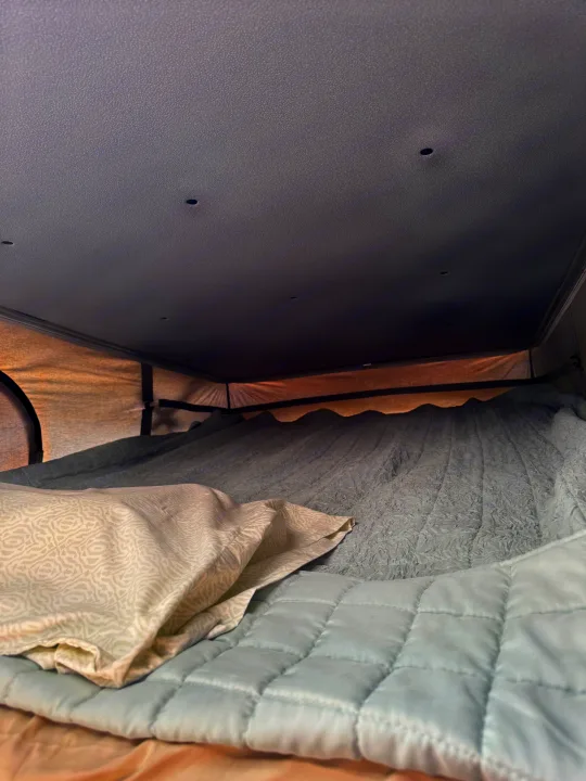 Inside an RV rental: a cozy bed with a patterned pillow, quilted blanket, and textured bedding under a ceiling with small lights.. Thor Motor Coach 18A Rize 2023