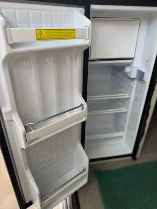 Empty, compact refrigerator inside an RV rental, showing internal shelves and door storage, ready for adventure supplies.. Thor Motor Coach 18A Rize 2023