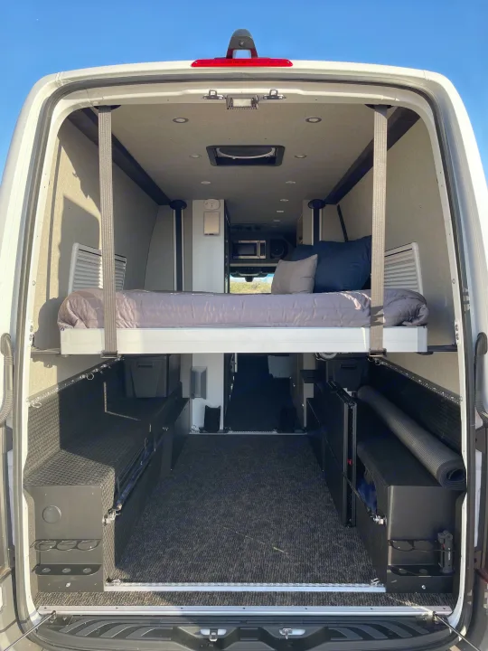 RV rental: Spacious camper van interior with an elevated bed, large storage area, and modern amenities.. Mercedes Sprinter 2023