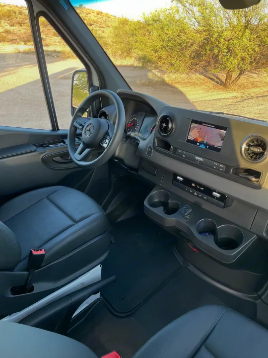 Interior of a modern rv rental van. Features Mercedes-Benz dashboard, steering wheel, and central screen with camera view.. Mercedes Sprinter 2023
