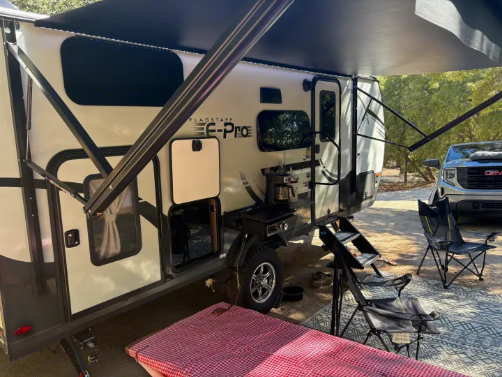 An RV rental, a Flagstaff E-Pro, extended with an awning, outdoor kitchen, and camping chairs at a scenic campsite.. FlagStaff E-PRO 20BH 2025