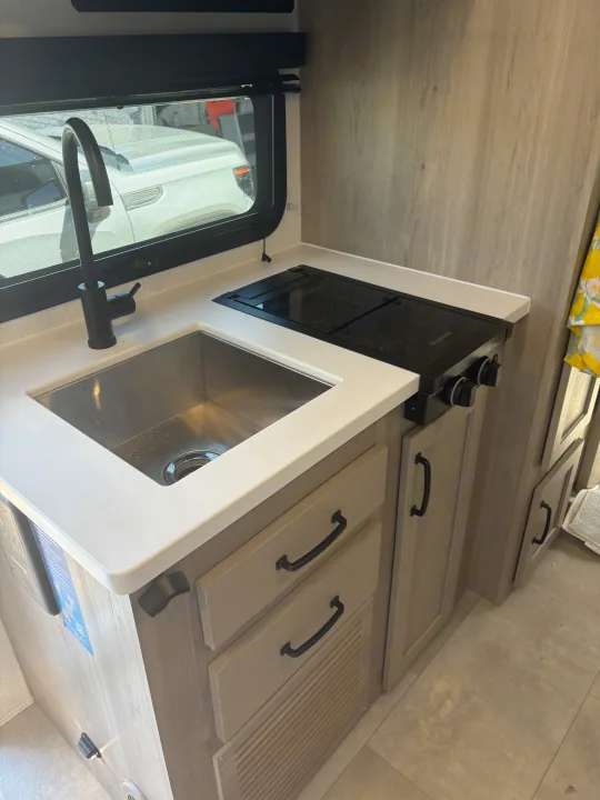 This RV rental kitchen features a bright, compact space with a stainless steel sink, black faucet, and two-burner cooktop, ready for adventures.. FlagStaff E-PRO 20BH 2025