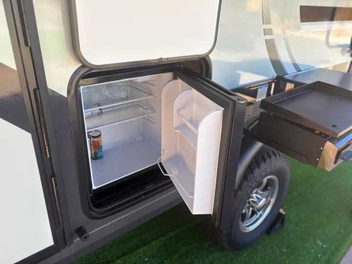 An RV rental's side compartment reveals an open mini-fridge and attached griddle, ideal for outdoor cooking.. FlagStaff E-PRO 20BH 2025