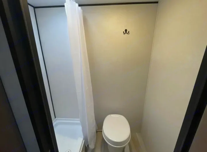 Compact RV rental bathroom: white toilet, shower with curtain, and wall hook. Practical and clean for your travels.. Other Other 2025