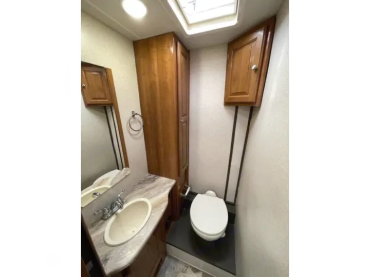 Inside this RV rental's bathroom: compact toilet, sink vanity, wooden cabinets, and a bright skylight.. Coachmen Leprechaun 2019