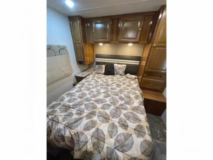 Experience comfort in this RV rental bedroom: cozy bed with leaf comforter, built-in wooden cabinets & storage.. Coachmen Leprechaun 2019