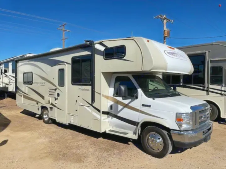 A white and tan Coachmen Class C RV, ideal for an rv rental, is parked outdoors on a sunny day.. Coachmen Leprechaun 2019