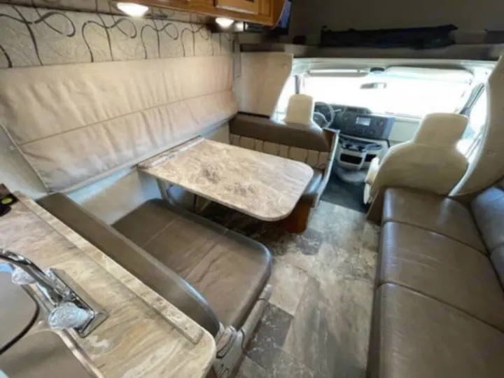 Step inside this RV rental, showcasing a comfortable dinette, functional kitchen, and bright cockpit area.. Coachmen Leprechaun 2019