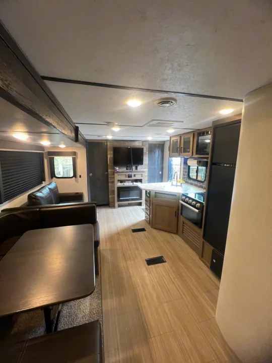 Modern rv rental interior with spacious living, dining, and full kitchen areas, featuring light wood floors and dark furniture.. Keystone RV Hideout 2021