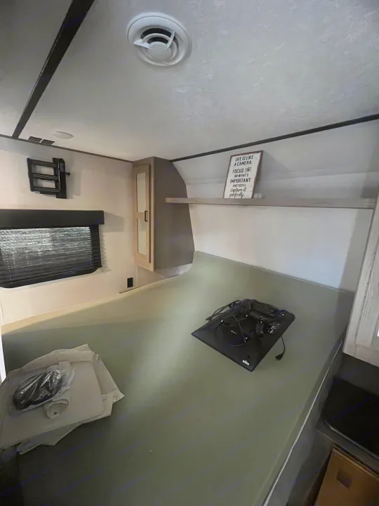 This RV rental bedroom features a grey mattress, window, TV wall mount, and overhead cabinet. Ideal for a comfortable stay.. Keystone RV Hideout 2021