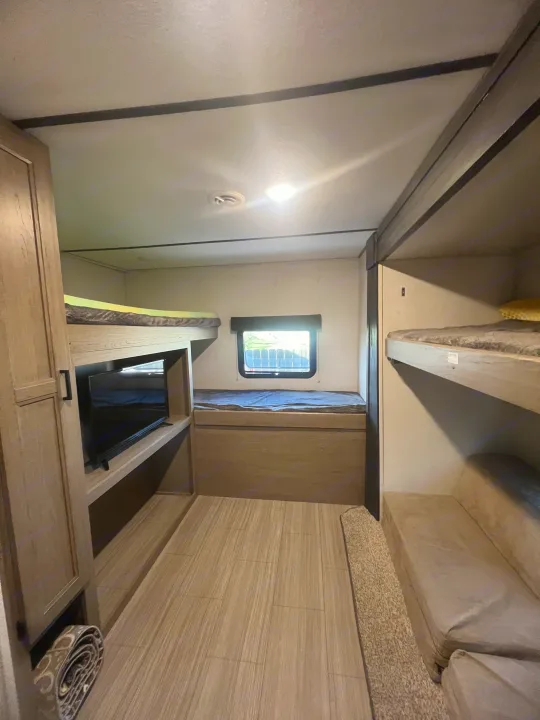 This RV rental interior features multiple bunk beds, a TV, and a cozy window nook, perfect for family travel.. Keystone RV Hideout 2021