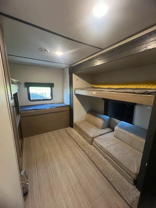 Spacious RV rental bunkhouse featuring multiple bunk beds, versatile seating, and ample natural light from windows.. Keystone RV Hideout 2021