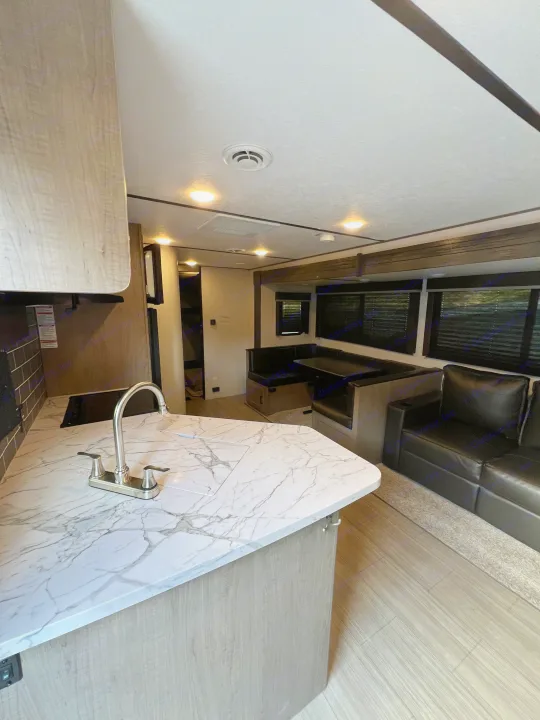 An RV rental interior shows a kitchen counter with sink, a dinette, and a sofa in a modern living space.. Keystone RV Hideout 2021