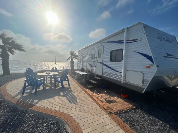 Enjoy your waterfront RV rental! This setup features a travel trailer, patio with chairs, and ocean views under a sunny sky.. Jayco Jay Flight 2010