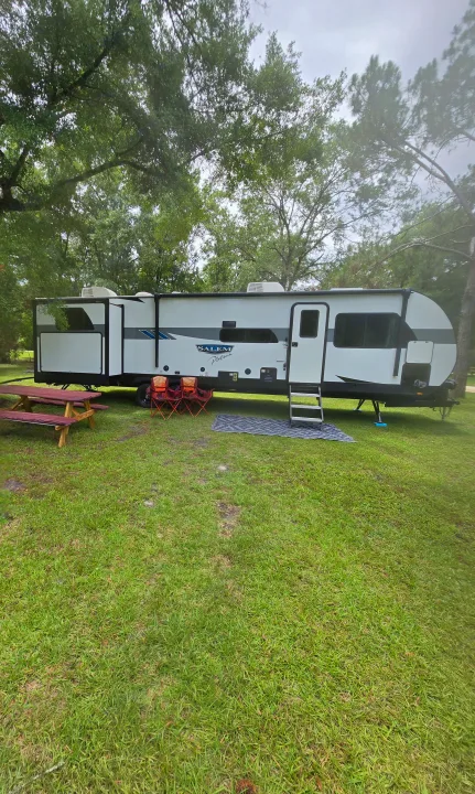 Perfect RV rental at a serene campground. A white travel trailer is set up on lush green grass with a picnic table and chairs.. Forest River Salem Platinum 2024