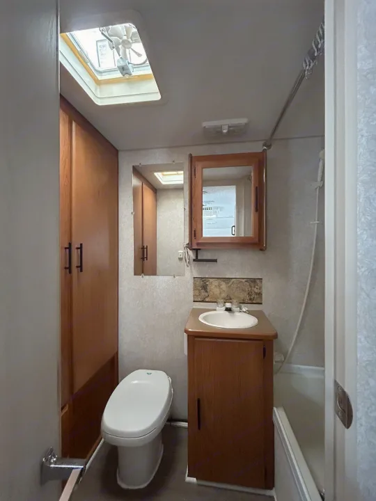 Compact RV rental bathroom: toilet, vanity with sink, shower, and storage, illuminated by a ceiling skylight.. Terry Dakota 722F 2004