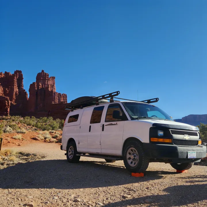White camper van, an ideal RV rental, parked in a scenic red rock desert for adventurous camping.. Chevrolet Express 1500 AWD 2014