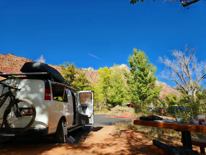 Adventure-ready RV rental: white van with bike rack at scenic red rock campsite with autumn trees.. Chevrolet Express 1500 AWD 2014
