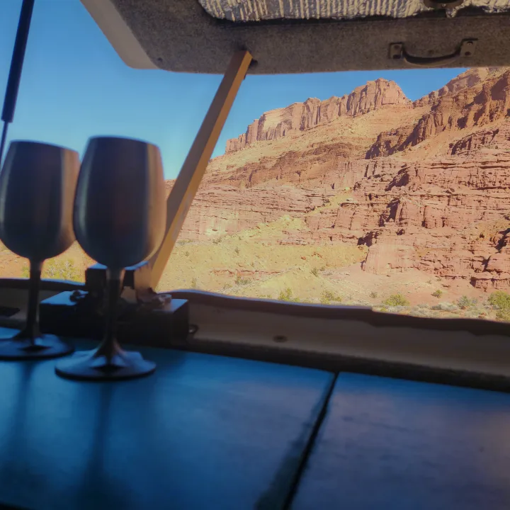 From an RV rental, two stemless wine glasses frame a view of a stunning red rock canyon under a clear blue sky. Serene desert landscape.. Chevrolet Express 1500 AWD 2014