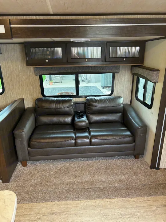 Spacious RV interior with a dark loveseat, cup holders, and overhead cabinets. Enjoy comfort during your next rv rental!. Cruiser RV Shadow Cruiser 2018