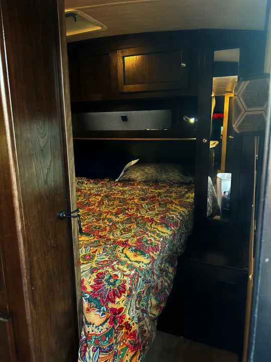 Explore the cozy RV rental bedroom interior, featuring a floral bedspread, wooden cabinets, and a compact mirrored space.. Cruiser RV Shadow Cruiser 2018