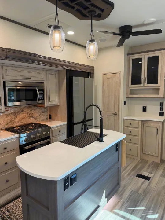 Spacious, modern RV rental kitchen featuring a large island, stainless appliances, pendant lights & wood-look finishes.. Forest River 3370RLS 2024