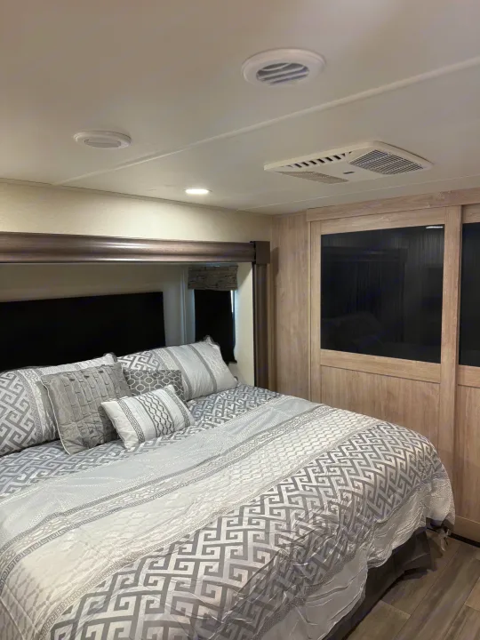 Spacious RV rental bedroom featuring modern gray and white bedding, built-in closet, and ceiling AC/vents for comfort.. Forest River 3370RLS 2024