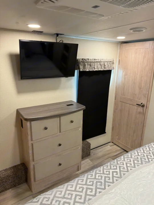 RV rental bedroom with mounted TV, dresser, and charging outlets. A compact, modern space ideal for your travels.. Forest River 3370RLS 2024