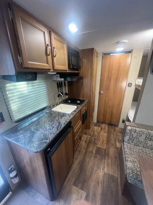 RV rental interior: compact kitchen features sink, stove, microwave, wood cabinets, and nearby dinette.. Keystone RV Summerland Mini 2017