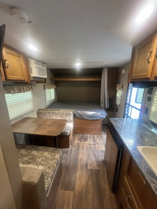 Cozy RV rental interior featuring a dinette, comfortable bed, compact kitchen counter, and AC unit.. Keystone RV Summerland Mini 2017