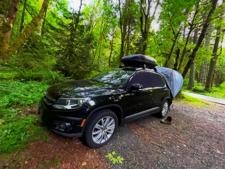 Black SUV with roof box and tarp for car camping in a lush forest, an ideal setup without an RV rental.. Volkswagen Tiguan 2012