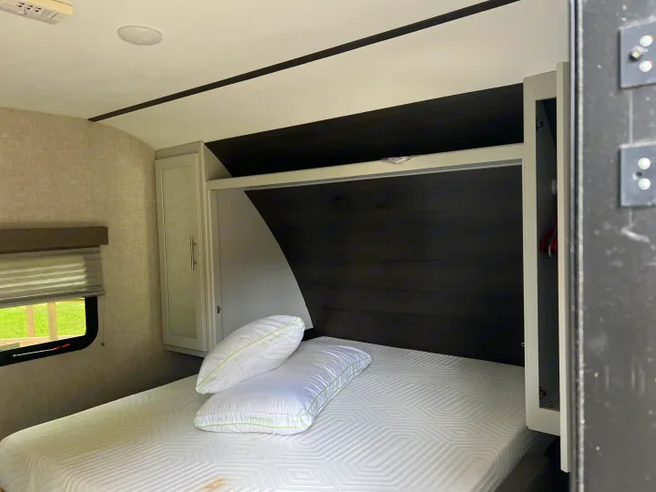 Cozy RV rental bedroom featuring a comfortable bed with fresh pillows, dark wood headboard, and convenient storage cabinets.. Keystone RV Bullet Crossfire 2019