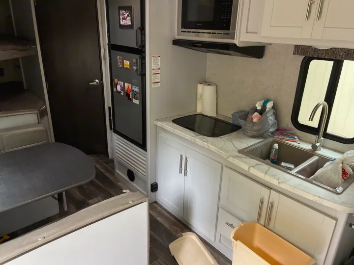 RV rental interior: kitchen with stove, sink, microwave, and fridge, plus bunk beds and a dinette table.. Keystone RV Bullet Crossfire 2019